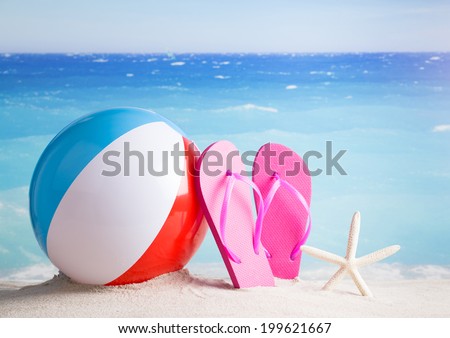 Beach ball, flip flops, starfish on sandy beach against blue ocean