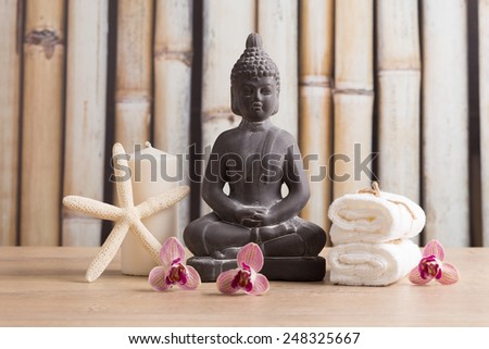 Grey Buddha statue, starfish, candle, towels, orchid flowers on bamboo background - spa concept
