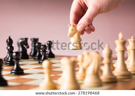 Conceptual image depicting making a strategic move with a hand moving a chess piece on a chessboard during a game of skill