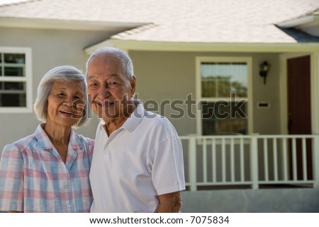 Grandma and Grandpa in foreground and a house on the background during the day.