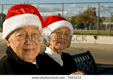 Side image of grandma and grandpa to the left of the frame as they smile for the camera as they wear Santa Clause hats.