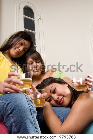 3 friends holding drinks while one female has her head on her friends leg. Two girls looking at the girl with her head down.
