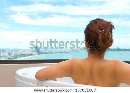 Backside woman in bathtub looking sea view