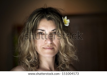 An attractive woman with long hair and flower frangipani in her hair looking up and smiling