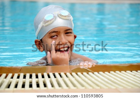 Smart Asian boy playing in the swimming pool wearing swimming hat and swimming goggles.