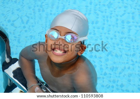 Smart Asian boy playing in the swimming pool wearing swimming hat and swimming goggles.
