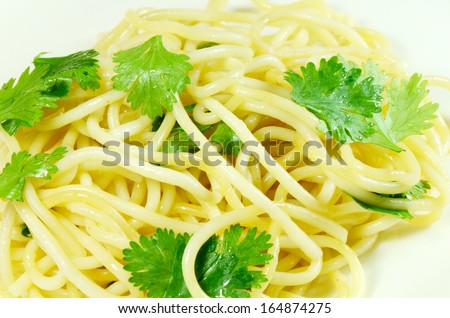 Boiled spaghetti cooked with organic olive oil and coriander leaves in a serving dish.