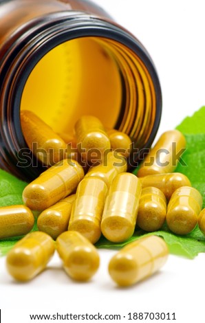 Turmeric Powder in Transparency Hard Gelatin Capsules Contain in Amber Glass Light resistant Bottle Displayed with Green Natural Leaves on White Background.