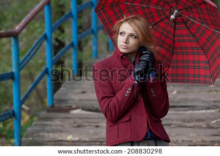 Pretty blond girl in stylish red jacket posing under the checkered umbrella