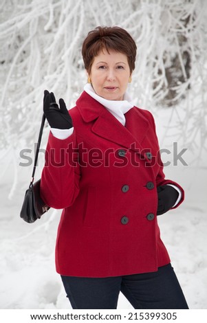 Attractive elderly woman in red coat posing on winter snowy street
