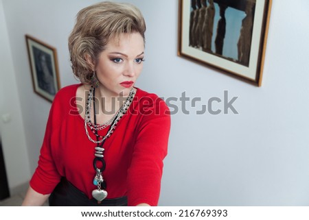 Beautiful blonde woman in full length in the red sweater poses against a wall with pictures