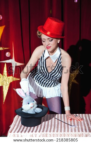 Circus artist woman magician pulls out a toy rabbit from hat