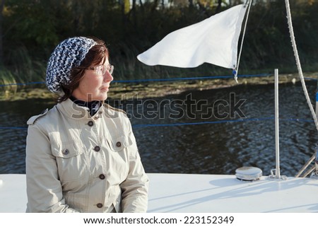Elderly woman yachtsman looks afar on a sailing yacht at sunny day