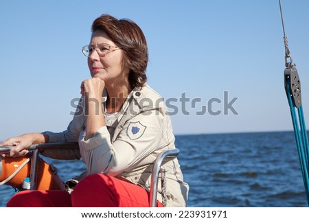 Elderly woman yachtsman sitting on the stern of sailing yacht at sunny day