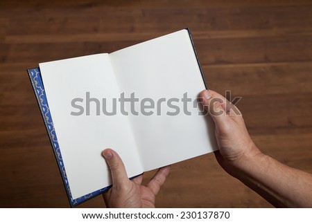 Male hands holding an open book on a background of the wooden floor