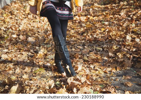Slender legs of a teenage girl walking on yellow fallen leaves at sunny autumn day