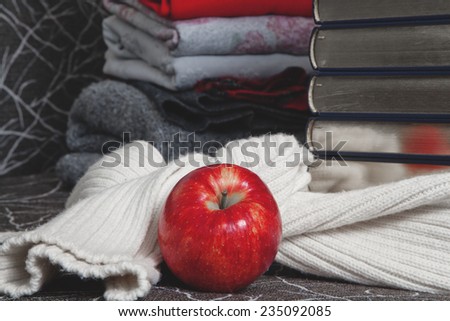 Composition of reading and relaxation at winter evenings. Stack of books with glossy edge wrapped in warm scarf and red apple foreground