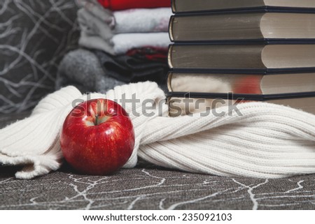 Composition of reading and relaxation at winter evenings. Stack of books with glossy edge wrapped in warm scarf and red apple foreground