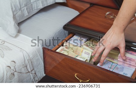 Hand reaches for the money in bedside table filled with Ukrainian cash