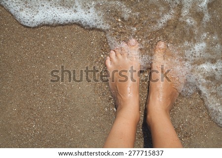 Two female bare feet on wet sand in the sea foam
