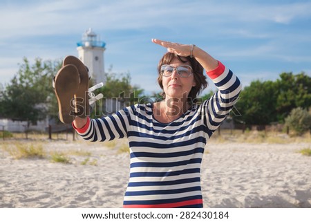 Beautiful elderly woman in a striped dress on the beach at background of old lighthouse