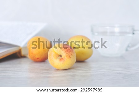 Summer set for an enjoyable vacation.  Still life with three ripe apricots, book and a cup of clear water.