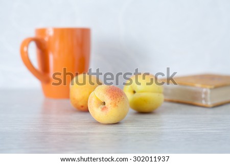 Summer set for lovers of reading.  Three apricots on gray table next to the book and orange cup