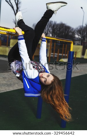 Beautiful girl doing gymnastics in the open air and hanging upside down