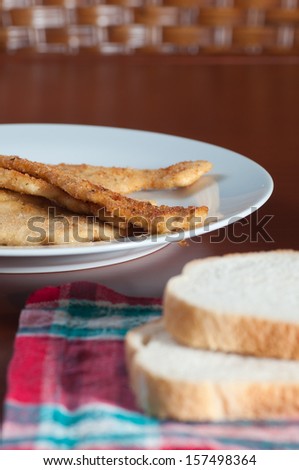 Breaded chicken steaks in a plate, bread and napkin in the table