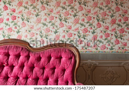 Old damaged red couch in an antique house. Flowers wallpaper in the wall