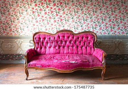 Old damaged red couch in an antique house. Flowers wallpaper in the wall