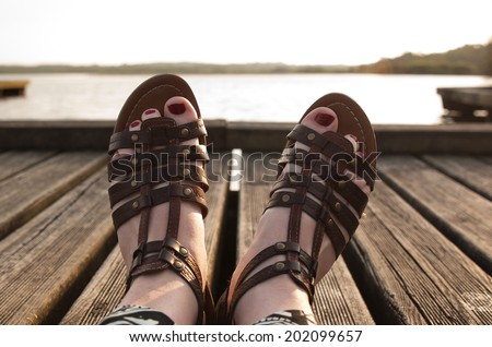 Woman feet in sandals and red nails in a wooden pier