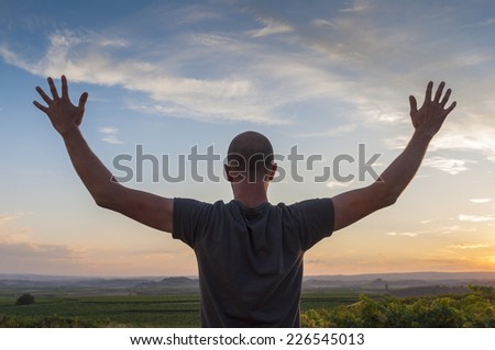 Young man, hands up, sowing happiness at sunset in nature setting