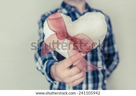 Man in plaid shirt holding a fabric heart with a red ribbon. Valentine\'s day