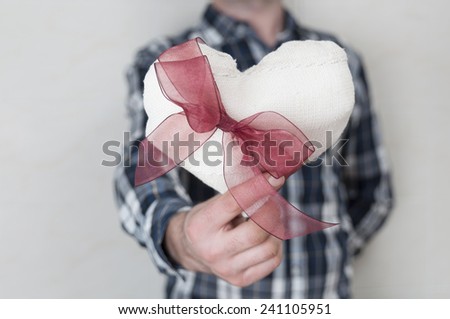 Man in plaid shirt holding a fabric heart with a red ribbon. Valentine's day