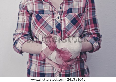 Woman in plaid shirt holding a fabric heart with a red ribbon. Valentine\'s day