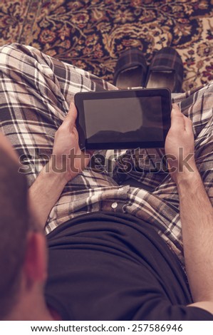 Man in pajamas sitting in the sofa and looking to the tablet