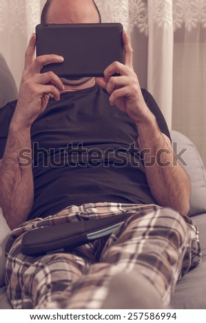 Man in pajamas sitting in the sofa and looking to the tablet