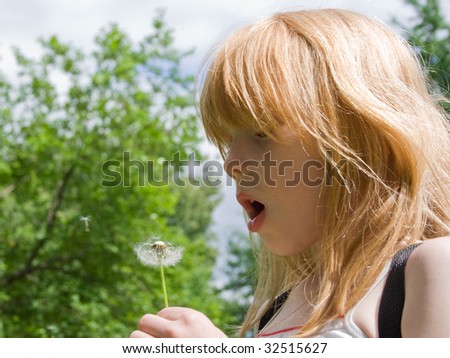 The red girl considers a dandelion on a glade in the afternoon