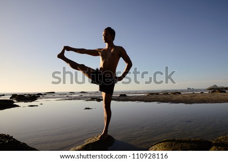 Asian man standing on one leg in yoga pose and one of his hand stretching with another leg.