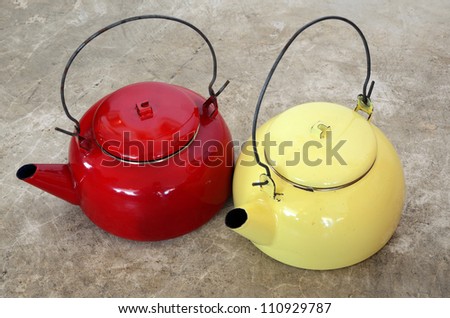 Red and yellow vintage metallic kettles on cement floor.