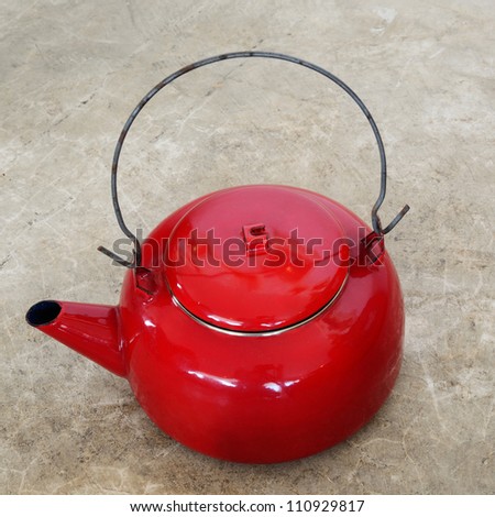Red vintage metallic kettle on cement floor.