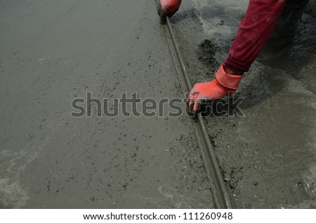 Worker troweling and spreading wet cement.
