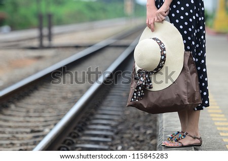Woman carrying her bag and hat waiting for train at railway station.