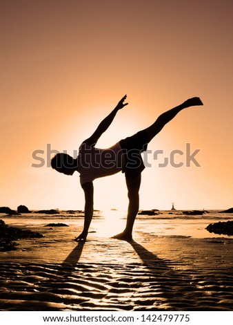 Asian man playing yoga on the beach, standing on one\'s leg, silhouetted the sunrise. The scene sets in Hua Hin, Thailand.