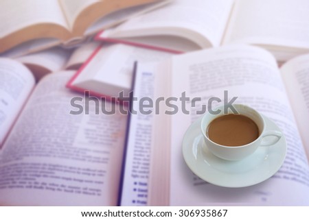 Hot coffee cup on book background in education or reading concept. Selecting focus on coffee cup with blur effect on book with vintage style.