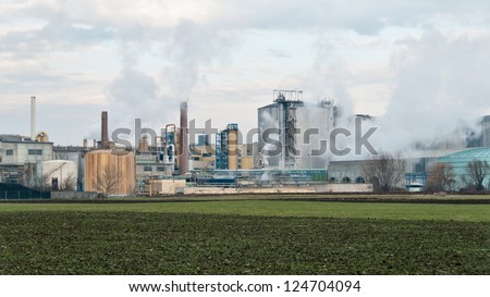 A sugar mill factory creating smoke in front of a cloudy sky