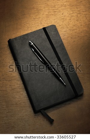 Black notepad and pen on table