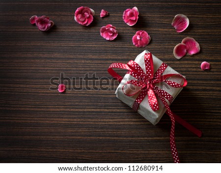 gift box on wooden table. Sweet holiday background with rose petals, curved ribbon./Valentines day background