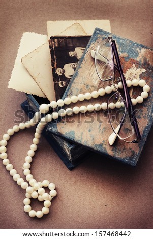 retro picture of a necklace lying on a book with glasses/ /romantic vintage background with and old pictures